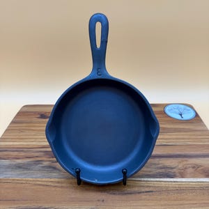 May include: A small, black cast iron skillet with a single handle and a loop for hanging. The number "3" is embossed on the handle. The skillet is displayed on a wooden cutting board.