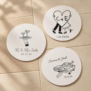 以下が含まれることがあります： 黒い線画が描かれた3枚の白い円形コースター。1枚は飲み物を乗せたトレイを持つ手と「Mr. & Mrs. Smith 10.12.26」の文字。もう1枚はハートを持つカップルと「C+E」「1.12.2026」。3枚目は車と「Emma & Jack」「10.12.26」が描かれています。