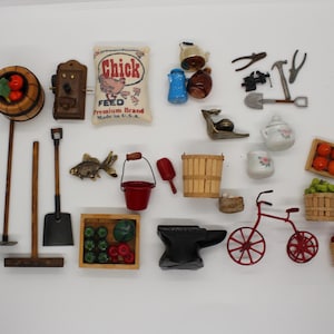 May include: A collection of miniature items including a wooden barrel, a Chick Feed bag, a wall telephone, garden tools, a red bucket, a bicycle, an anvil, crates of fruit, a fish figurine, and various small household objects arranged on a white surface.