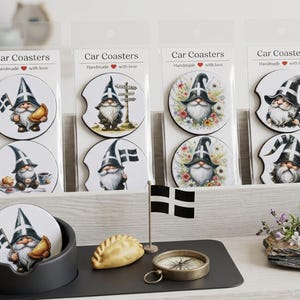 May include: Five sets of round car coasters in clear plastic packaging, each featuring gnome illustrations with the Cornish flag. One set displays the text My a gar Kernow. A black coaster holder, a pasty figurine, and a small flag are on display.