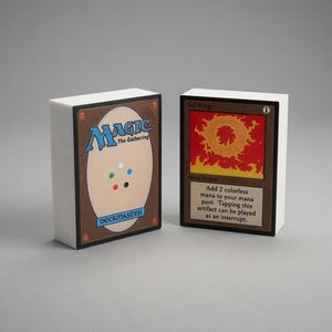 May include: A deck of Magic The Gathering cards with white edges. One card shows the back design with the text Magic The Gathering Deckmaster. The other card is a Sol Ring artifact card with a red sun illustration and text describing its mana ability.