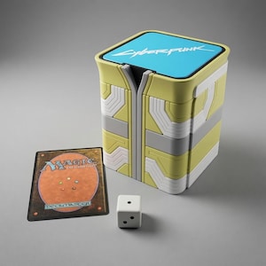May include: A square deck box featuring a yellow and white geometric pattern with a bright blue top lid displaying the word Cyberpunk in white text. Beside the box is a Magic The Gathering card back and a single white six-sided die with black pips.