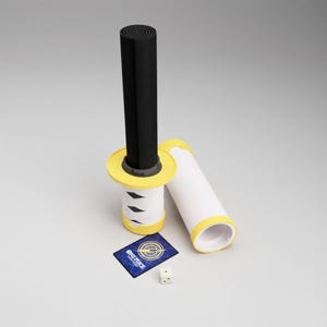May include: A black and yellow sword-like object with a white handle wrapped with black accents. A white tube with yellow trim lies next to it. A blue card with "ONE PIECE" text and a die are also present.