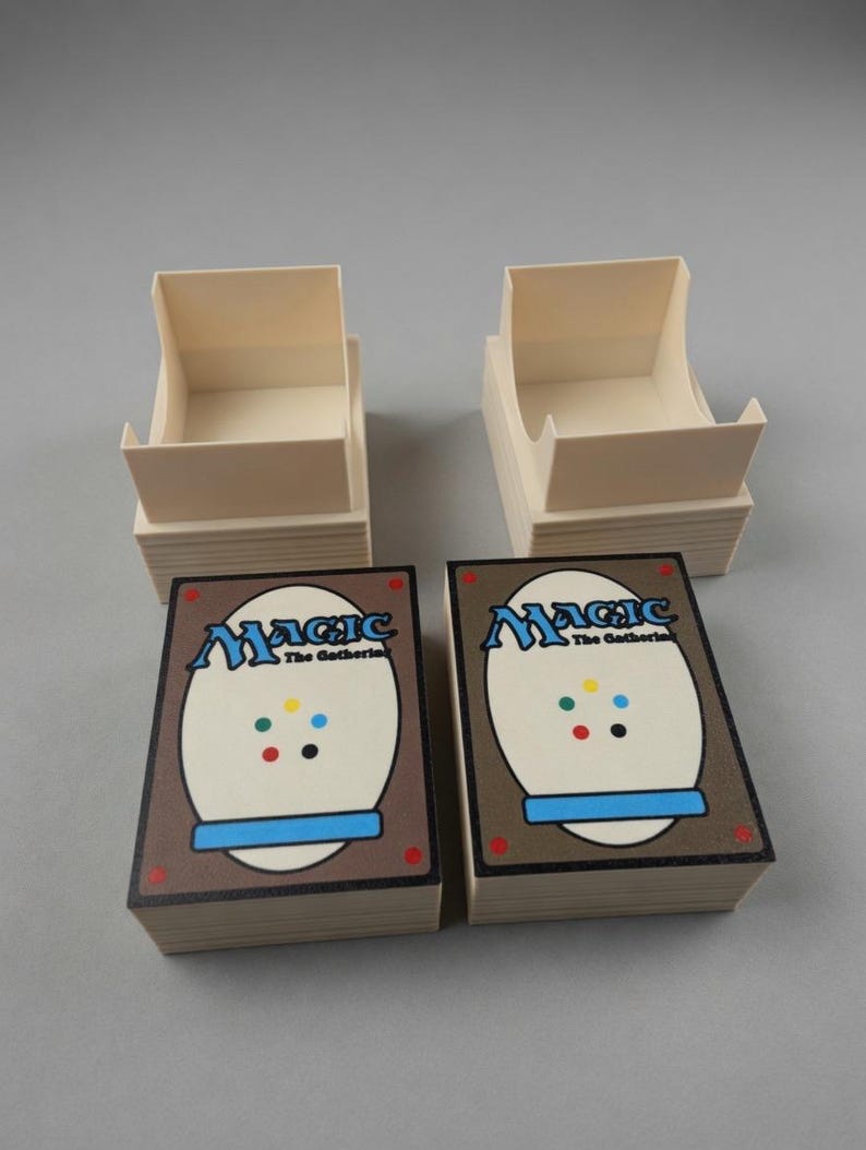May include: Two stacks of Magic: The Gathering playing cards with the card backs visible, featuring the game's logo and a brown border. Two beige card storage boxes are positioned above the card stacks, ready for use.