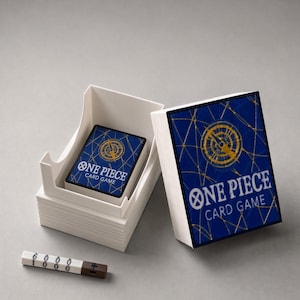 Peut inclure: Une boîte de rangement en plastique blanc contenant un jeu de cartes One Piece Card Game avec un motif de boussole bleu et or. Le couvercle présente le même motif. Un petit compteur blanc et marron avec les chiffres 6000 et 1000 est inclus.