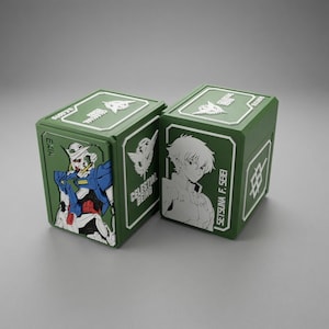 May include: Two olive green rectangular storage boxes featuring white and coloured relief designs. One box displays a blue and white robot labelled EXIA, while the other shows a white character profile labelled SETSUNA F. SEIEI and CELESTIAL BEING text.