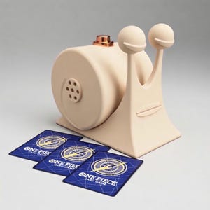 Può includere: Un porta carte a forma di lumaca beige con una parte superiore color rame e due antenne sferiche. Tre carte blu di "One Piece Card Game" sono davanti al supporto. La lumaca ha un corpo circolare con una serie di fori e una faccia sorridente.