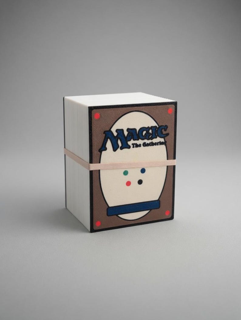 May include: A white, rectangular box of Magic: The Gathering trading cards, secured with a light brown rubber band. The box features a brown and cream-colored design with the word "Magic" in blue.