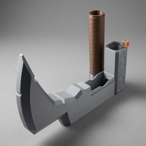 May include: A grey, axe-shaped dice tower featuring a brown, textured cylindrical handle and a vertical compartment for rolling dice. A small, light-coloured wooden die with the number 5 printed in red sits on the top edge of the tower structure.
