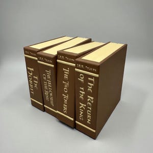 以下が含まれることがあります： J.R.R.トールキンによる4冊の茶色の本。タイトルは「The Hobbit」、「The Fellowship of the Ring」、「The Two Towers」、「The Return of the King」。各本は、金色の文字が刻まれた茶色の背表紙と、クリーム色のページ端が特徴です。