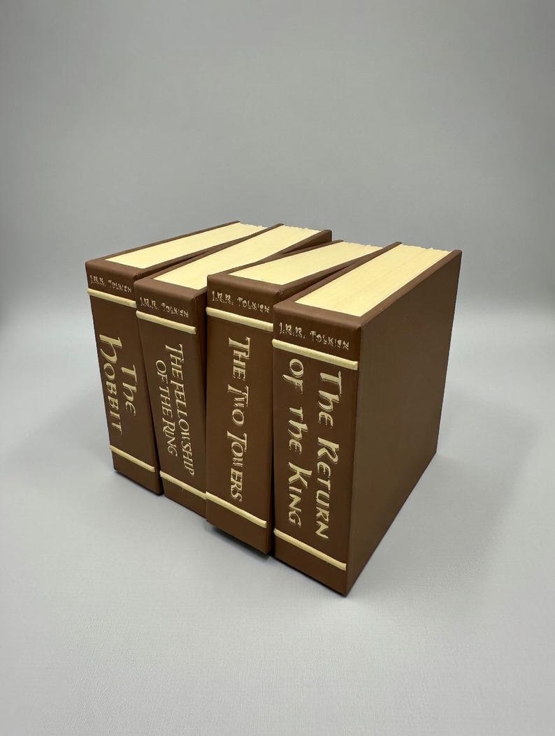 以下が含まれることがあります： J.R.R.トールキンによる4冊の茶色の本。タイトルは「The Hobbit」、「The Fellowship of the Ring」、「The Two Towers」、「The Return of the King」。各本は、金色の文字が刻まれた茶色の背表紙と、クリーム色のページ端が特徴です。