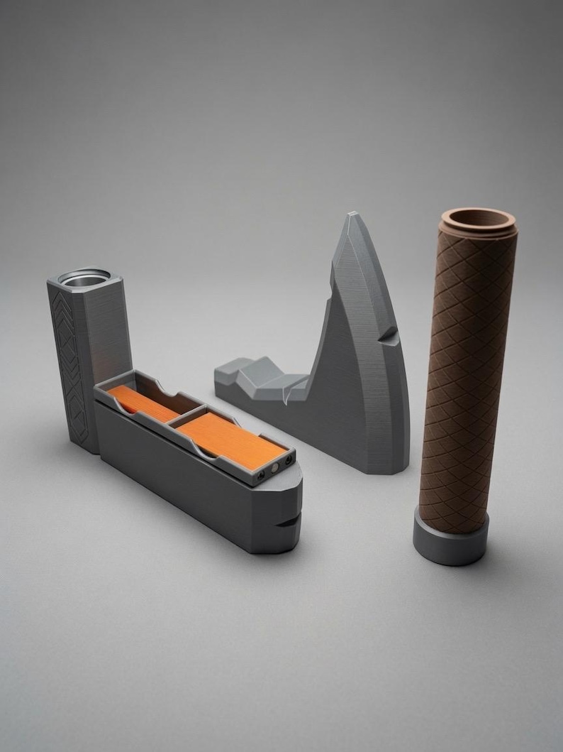 May include: A set of three grey and brown objects including a rectangular grey container with two orange interior compartments, a grey angular wedge-shaped piece with a pointed top, and a cylindrical brown textured handle with a grey base.