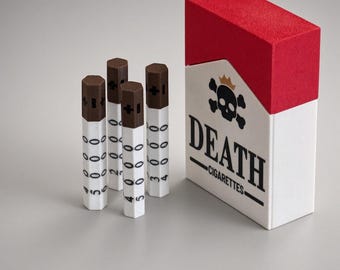 May include: A rectangular white and red box labeled DEATH CIGARETTES with a black skull and crown graphic, accompanied by four hexagonal white and brown sticks. Each stick features a brown top with a plus sign and vertical columns of numbers.