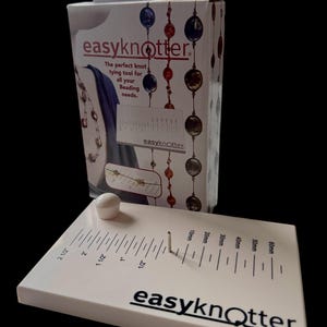 May include: A white Easy Knotter beading tool with a white knob and a metal pin. The tool has measurements in inches and millimeters. The packaging box is white with the text "easyknotter" and a graphic of beaded jewelry.