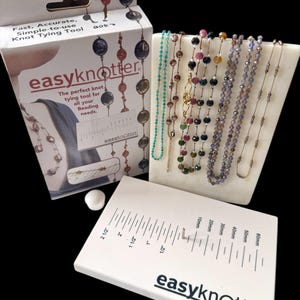 May include: A white Easy Knotter tool kit with a ruler, a white display stand with beaded necklaces, and a box with the text "Fast, Accurate, Simple-to-use Knot Tying Tool". The ruler measures up to 2 1/2 inches.