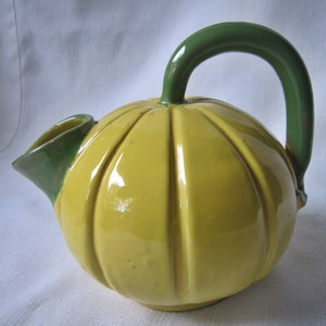 May include: A yellow ceramic pitcher shaped like a pumpkin with a green handle and spout.