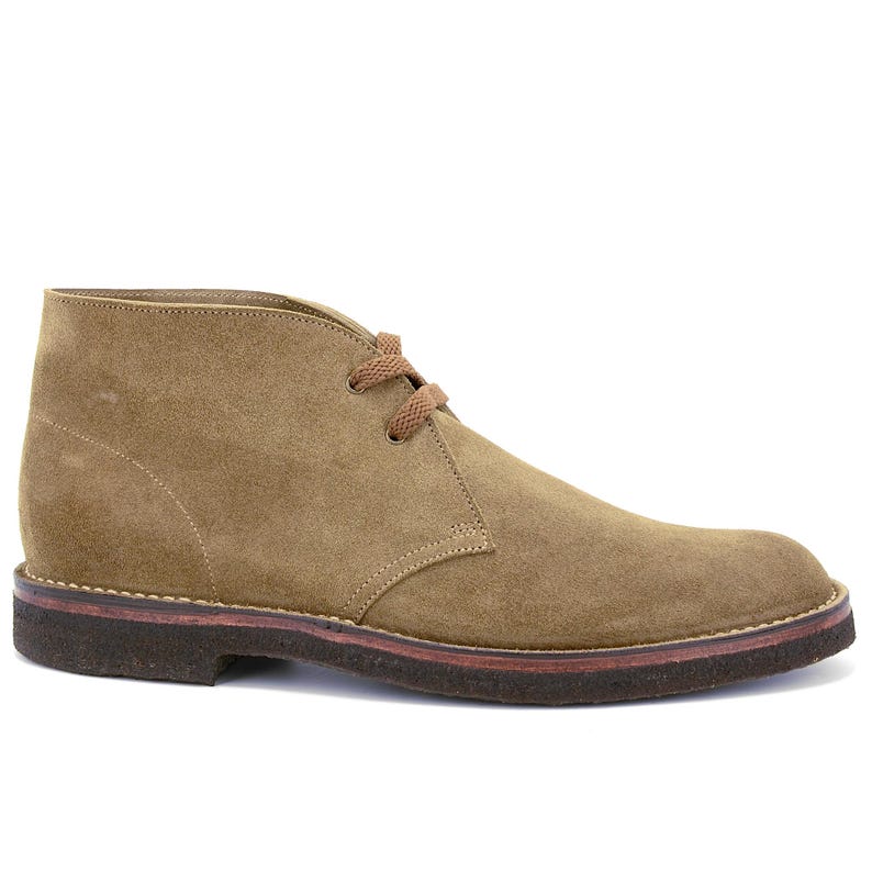 May include: A tan suede chukka boot with brown laces and a dark brown sole. The ankle-high boot features a rounded toe and a stitched design along the seams. The shoe is designed for casual wear.