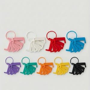 May include: A selection of keyrings in a variety of colours, each with a fan-shaped design and a metal ring. The keyrings are in shades of pink, white, red, blue, purple, teal, orange, yellow, and black.