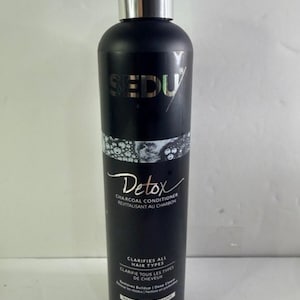 Könnte beinhalten: Eine schwarze Flasche SEDU Detox Aktivkohle-Conditioner. Die Flasche hat einen silbernen Deckel und weißen Text mit der Aufschrift "Detox" und "Clarifies All Hair Types". Die Flasche enthält 300 ml Produkt.