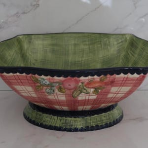 May include: Ceramic serving bowl with a green and red plaid pattern. The interior is green, and the rim is scalloped with a dark blue trim. Features two dark blue handles and a decorative base. The bowl is decorated with fruit and vegetable motifs.