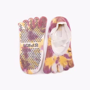 Peut inclure: Chaussettes à doigts tie-dye dans les tons de jaune, violet et blanc. Les chaussettes ont des fentes individuelles pour les orteils et un motif antidérapant sur les semelles. Le mot "UPRA" est imprimé sur la semelle. Idéales pour le yoga ou le Pilates.