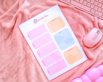 May include: A pink daily plan notepad with sections for tasks, notes, and reminders. A pink computer mouse and keyboard are next to the notepad on a pink blanket. The notepad has the words "Daily Plan" at the top.
