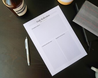 May include: A white "Daily Reflection" worksheet with prompts for gratitude and goals, alongside a pen, notebook, and a bottle of Aesop product on a dark surface. The worksheet is blank.