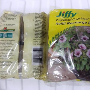 May include: Two packages of Jiffy Professional Greenhouse Refill Recharge Rellenc. The yellow package features a photo of purple petunias in a pot. The other package is white and has text in Spanish and English.