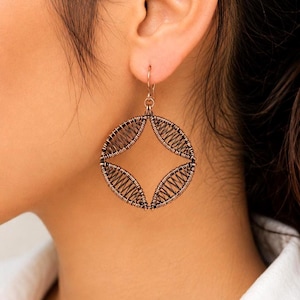 May include: A copper-toned wire-wrapped earring featuring a circular frame with four distinct leaf-shaped sections filled with intricate, tightly coiled wire patterns. The earring hangs from a simple hook, showcasing a metallic finish and detailed craftsmanship.
