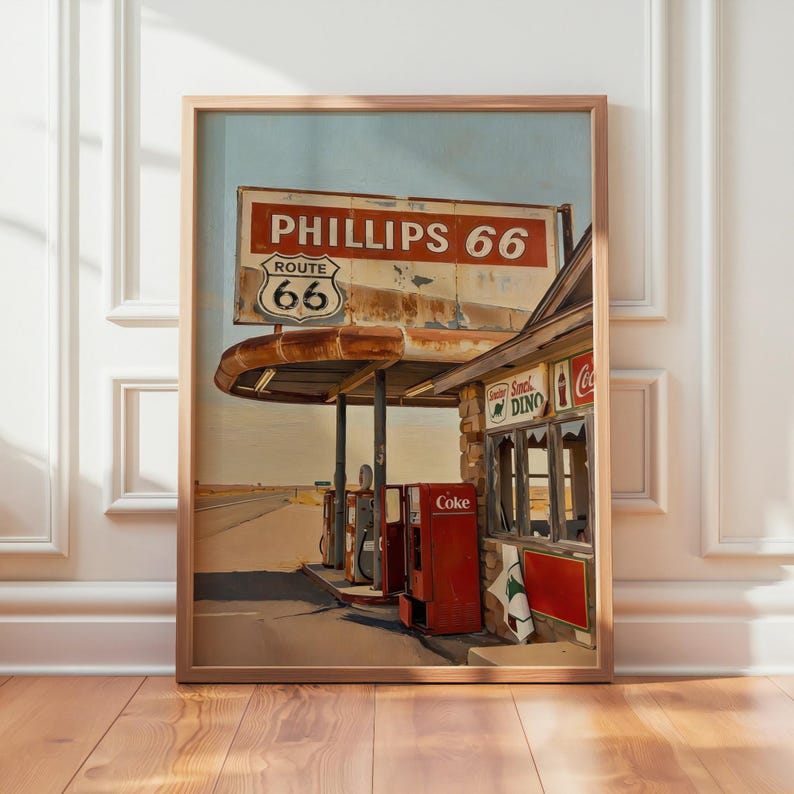 May include: Framed print of a vintage Phillips 66 gas station on Route 66. The sign displays "Phillips 66" and "Route 66". A red Coke machine and petrol pumps are visible. The artwork is in a wooden frame.