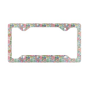Peut inclure: Un cadre de plaque d'immatriculation rectangulaire orné d'un motif répétitif de casse-noisettes, de feuillage vert et de fleurs de poinsettia roses. Le design inclut des petits cadeaux et des éléments décoratifs sur fond blanc.