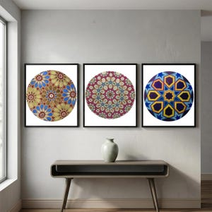 May include: Three framed circular art prints with intricate geometric patterns. The prints feature a variety of colors, including gold, blue, red, and yellow, set against a white background. The frames are black, and the artwork is displayed on a neutral-colored wall.