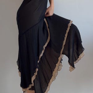 Peut inclure: Robe noire avec un col bénitier et des bretelles spaghetti. La robe présente une jupe superposée avec une bordure beige à volants. La modèle porte des talons hauts jaunes. La robe est en tissu transparent.