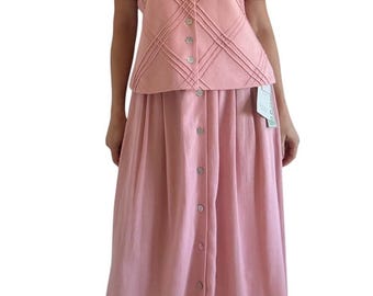 May include: A light pink two-piece set consisting of a short-sleeved blouse and a long skirt. The blouse features a round neckline, shoulder pads, and a diagonal stitched grid pattern with a front button closure. The matching skirt has a button-down front.
