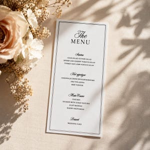 May include: A vertical white menu card with a black double-line border and black serif text. The text lists sections for The Menu, Starters, Hot appetizer, Main Course, and Dessert, featuring various food items like crab salad and filet mignon.