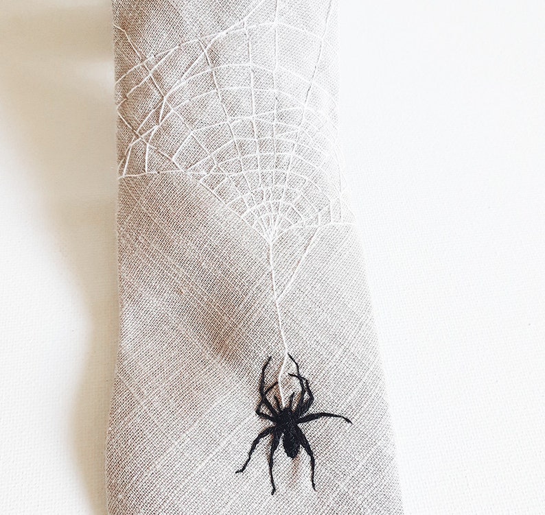 Eine beige Krawatte mit einem weißen gestickten Spinnennetz und einer schwarzen gestickten Spinne, die am Netz hängt.
