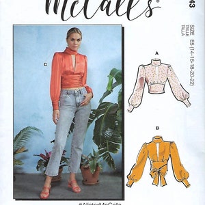 May include: McCall's sewing pattern M8043 features multiple top designs. The image shows a model wearing a rust-colored top with a keyhole neckline and long sleeves. Also shown are illustrations of two other top styles.