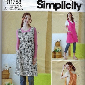 May include: Simplicity sewing pattern R11758 for an apron with a square neckline and side pockets. The pattern displays three variations: a black and white floral print, a solid pink, and an orange polka dot design, all worn over casual clothing.