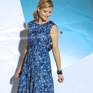 May include: A sleeveless blue floral print dress with a tiered skirt. The dress features a fitted bodice and a knee-length hemline. The model is wearing blue high-heeled sandals and a dark bracelet. The background is a gradient of blue and white.