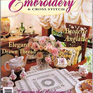 May include: The cover of an "Embroidery & Cross Stitch" magazine features a table setting with a white lace tablecloth, a teapot, teacups, and a floral arrangement. The magazine title is in pink script, with text that reads "Elegant Drawn Thread" and "Creating the Heirlooms of Tomorrow."