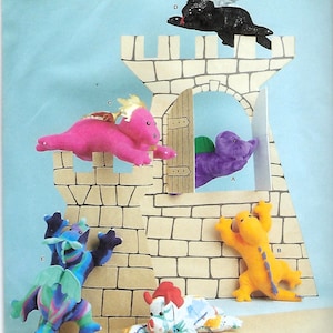 May include: Simplicity sewing pattern R11982 for plush dragon toys. The cover features a cardboard castle display with six stuffed dragons in various colors including pink, purple, yellow, black, blue-green, and a white multi-colored pattern.