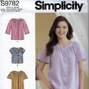 May include: Simplicity sewing pattern S9782 for sizes 18-26. The envelope features illustrations of three button-front blouses with gathered necklines and various sleeve lengths, alongside a photograph of a light purple blouse with short sleeves.