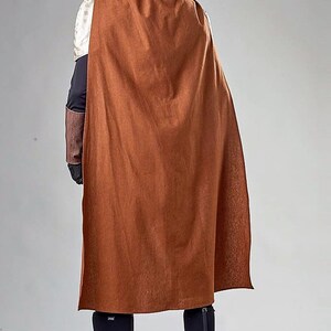 Pu&ograve; includere: Un mantello marrone con cappuccio e collo alto. Il mantello &egrave; realizzato in un tessuto morbido e testurizzato e ha un design lungo e fluido. La persona che indossa il mantello &egrave; in piedi con le spalle alla telecamera.