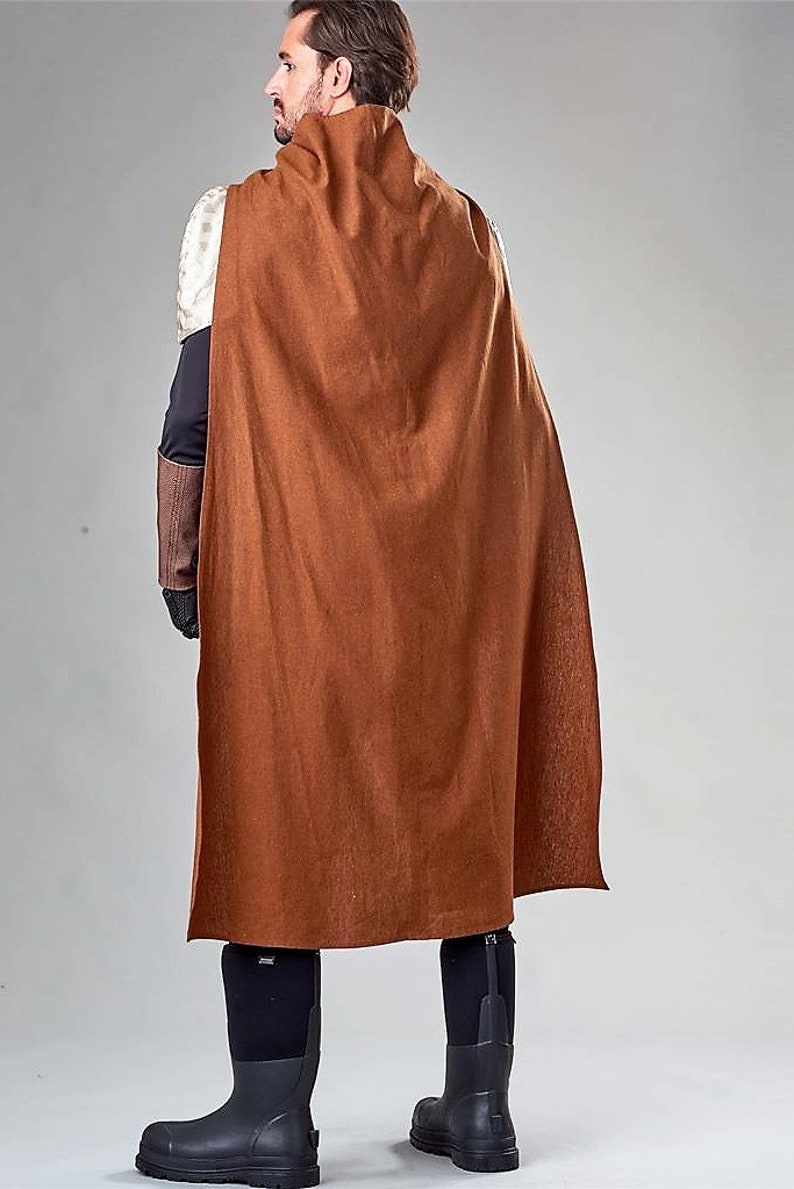 Pu&ograve; includere: Un mantello marrone con cappuccio e collo alto. Il mantello &egrave; realizzato in un tessuto morbido e testurizzato e ha un design lungo e fluido. La persona che indossa il mantello &egrave; in piedi con le spalle alla telecamera.