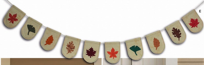 May include: A decorative bunting banner featuring ten beige fabric pennants suspended on a white string. Each pennant displays a unique, colorful leaf print in shades of red, orange, dark green, and brown, representing various tree species.