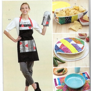 May include: Simplicity sewing pattern S9942 featuring a black apron with a patchwork pocket and matching oven mitt. The image also shows a tortilla warmer, a chip basket, and a placemat, all with colorful patchwork designs.