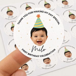 Puede incluir: Una pegatina redonda con la fotografía de un bebé sonriente que lleva un gorro de fiesta a rayas azules y amarillas con un pompón naranja. El texto dice THANK YOU FOR MAKING MY DAY SPECIAL, Milo y FIRST BIRTHDAY CELEBRATION con estrellas doradas.