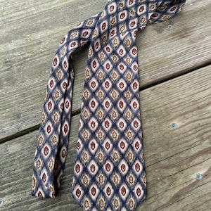 May include: A patterned necktie with a repeating diamond design in navy blue, beige, and burgundy. The tie is made of a smooth fabric and is displayed on a weathered wooden surface. The tie is a classic accessory.