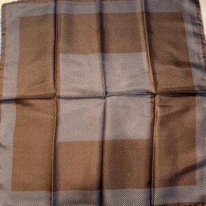 May include: A brown pocket square with a white dotted pattern and a solid brown border. The pocket square is folded, showcasing the design. The edges are a lighter shade of brown.