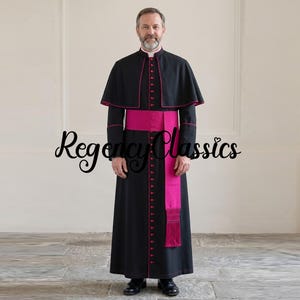 May include: A black cassock featuring a mandarin collar, a short shoulder cape, and a long sash in vibrant fuchsia. The garment is adorned with fuchsia piping along the edges and a vertical row of matching buttons. The text Regency Classics is visible.